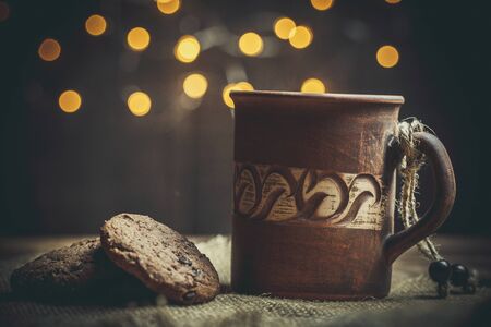 Brown clay vintage coffee mugs and delicious chocolate chip cookies on a wooden table in warm colors