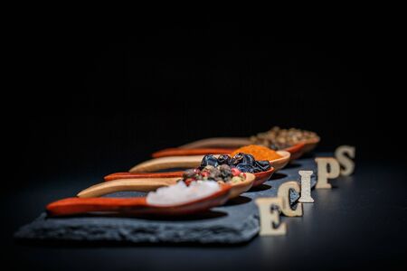 Different spices, peppers, coriander, sesame seeds and others for cooking are in wooden spoons on a...