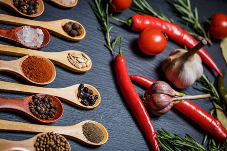 Spices in wooden spoons and cherry tomatoes, chili peppers, garlic and herbs for cooking on a black...