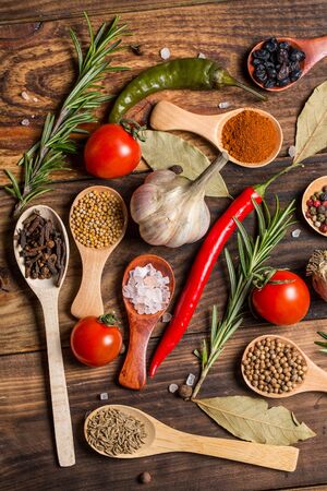 Different spices in wooden spoons and different ingredients for cooking, cherry tomatoes, garlic, coriander and red pepperの写真素材