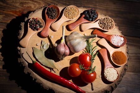 Different spices in wooden spoons and different ingredients for cooking, cherry tomatoes, garlic,...