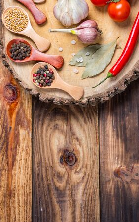 Different spices in wooden spoons and different ingredients for cooking, cherry tomatoes, garlic, coriander and red pepperの写真素材