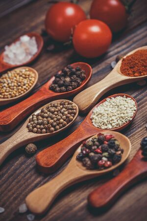 Different spices in wooden spoons and different ingredients for cooking, cherry tomatoes, garlic, coriander and red pepperの写真素材