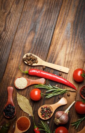 Different spices in wooden spoons and different ingredients for cooking, cherry tomatoes, garlic, coriander and red pepperの写真素材