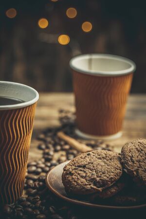 Cups and cups with coffee, coffee grains and gingerbread cookies nearby for refreshments in warm home colorsの写真素材