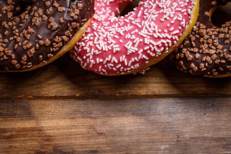Chocolate and pink fresh donuts on a wooden breakfast tableの写真素材