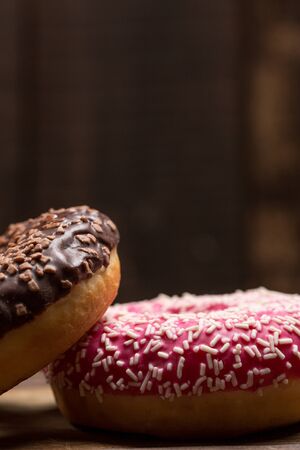 Chocolate and pink fresh donuts on a wooden breakfast tableの写真素材