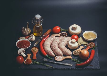 Raw sausages, different vegetables, spices and ingredients on a black backgroundの写真素材