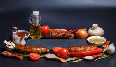 Grilled sausages, vegetables, hot peppers and various spices and ingredients on a black backgroundの写真素材