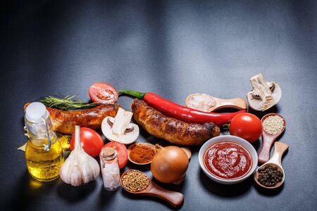 Grilled sausages, vegetables, hot peppers and various spices and ingredients on a black backgroundの写真素材