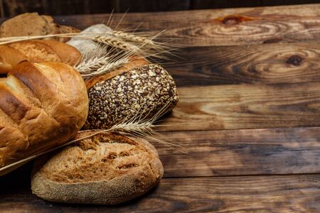 Different loaves of bread and rolls with wheat and flour on a wooden table