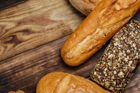 Different loaves of bread and rolls with wheat and flour on a wooden tableの写真素材
