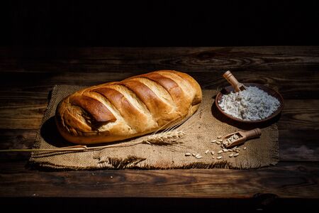 Different loaves of bread and rolls with wheat and flour on a wooden tableの写真素材