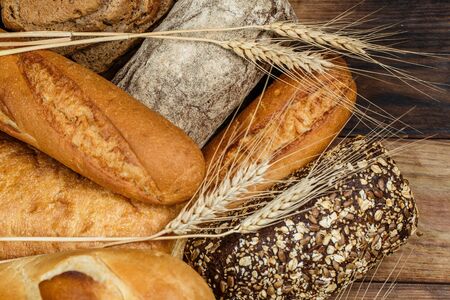 Different loaves of bread and rolls with wheat and flour on a wooden table