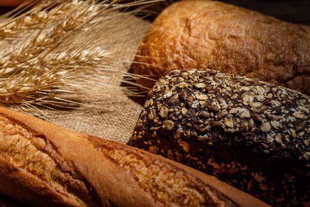 Different loaves of tasty bread with wheat, flour and gluten on a wooden tableの写真素材
