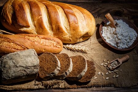 Different loaves of tasty bread with wheat, flour and gluten on a wooden tableの写真素材