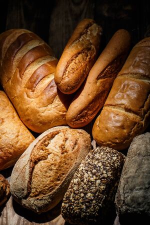 Different loaves of tasty bread with wheat, flour and gluten on a wooden tableの写真素材