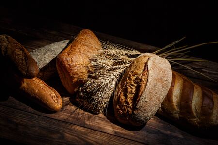 Different loaves of tasty bread with wheat, flour and gluten on a wooden tableの写真素材