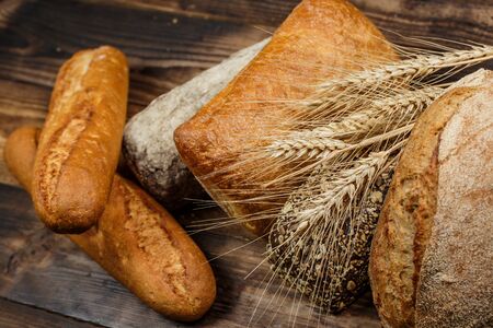 Different loaves of tasty bread with wheat, flour and gluten on a wooden tableの写真素材