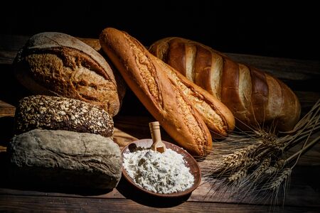Different loaves of tasty bread with wheat, flour and gluten on a wooden tableの写真素材