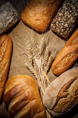 Different loaves of tasty bread with wheat, flour and gluten on a wooden table