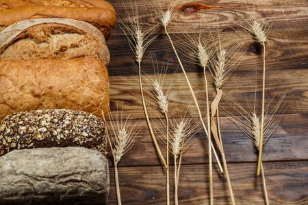 Different loaves of tasty bread with wheat, flour and gluten on a wooden tableの写真素材