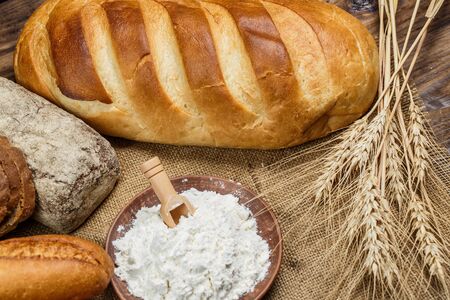 Fresh loaves of bread with wheat and gluten on a wooden table