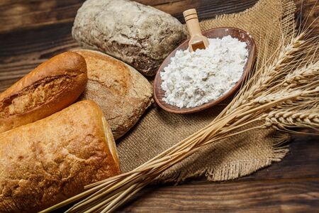 Fresh loaves of bread with wheat and gluten on a wooden table