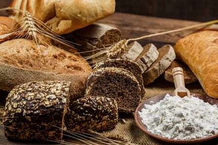 Fresh loaves of bread with wheat and gluten on a wooden tableの写真素材
