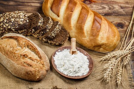 Fresh loaves of bread with wheat and gluten on a wooden table