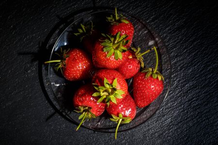 Ripe red strawberries on the dishes on a black backgroundの写真素材