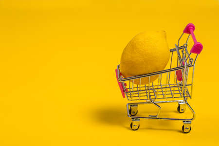 Yellow lemon in a shopping cart on a yellow background, shopping trolleyの写真素材
