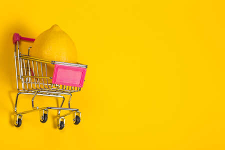 Yellow lemon in a shopping cart on a yellow background, shopping trolleyの写真素材
