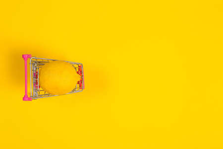 Yellow lemon in a shopping cart on a yellow background, shopping trolleyの写真素材