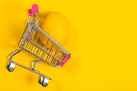 Yellow lemon in a shopping cart on a yellow background, shopping trolleyの写真素材