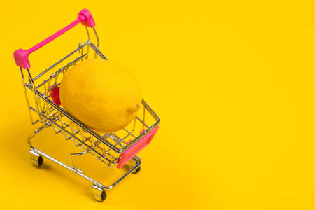 Yellow lemon in a shopping cart on a yellow background, shopping trolleyの写真素材
