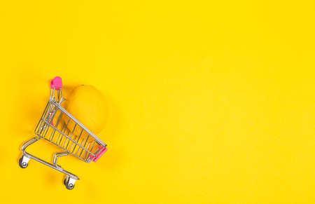 Yellow lemon in a shopping cart on a yellow background, shopping trolleyの写真素材