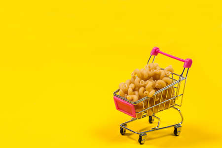 Pasta in a shopping trolley on a yellow backgroundの写真素材