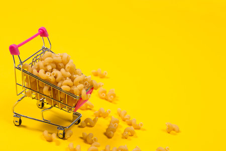 Pasta in a shopping trolley on a yellow backgroundの写真素材