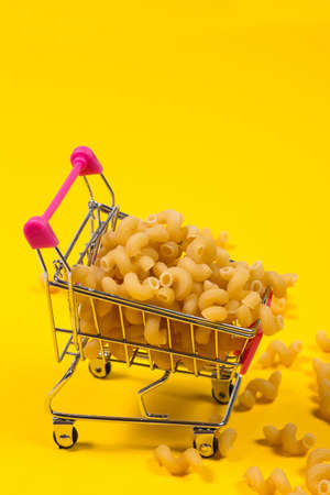 Pasta in a shopping trolley on a yellow backgroundの写真素材