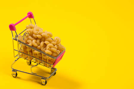 Pasta in a shopping trolley on a yellow backgroundの写真素材