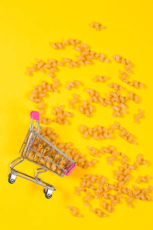 Pasta in a shopping trolley on a yellow backgroundの写真素材