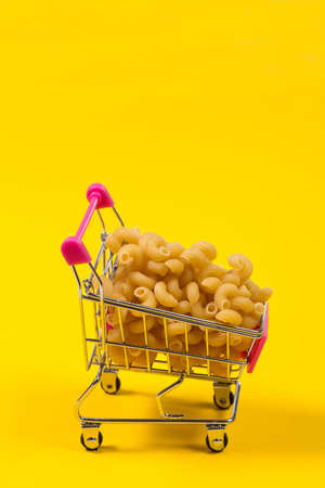 Pasta in a shopping trolley on a yellow backgroundの写真素材