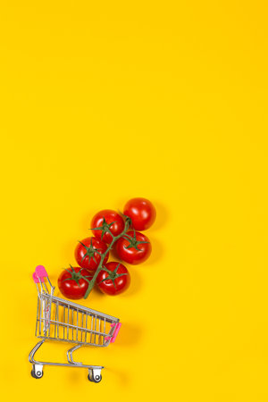 Cherry tomatoes and shopping cart on yellow backgroundの写真素材