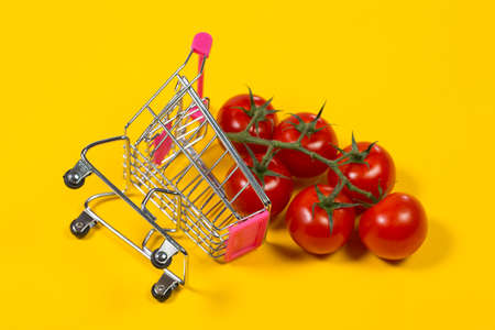 Cherry tomatoes and shopping cart on yellow backgroundの写真素材