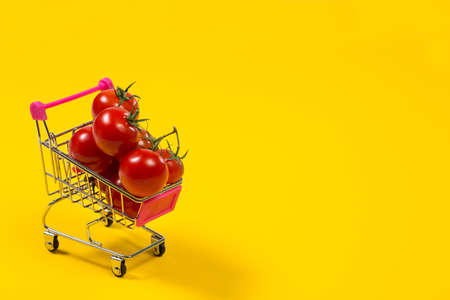 Cherry tomatoes and shopping cart on yellow backgroundの写真素材