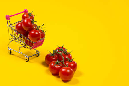 Cherry tomatoes and shopping cart on yellow backgroundの写真素材