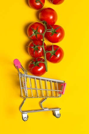 Cherry tomatoes and shopping cart on yellow backgroundの写真素材