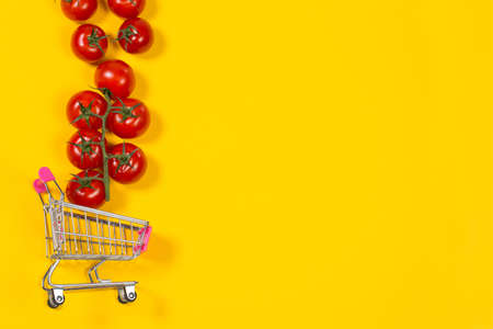 Cherry tomatoes and shopping cart on yellow backgroundの写真素材