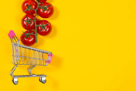 Cherry tomatoes and shopping cart on yellow backgroundの写真素材